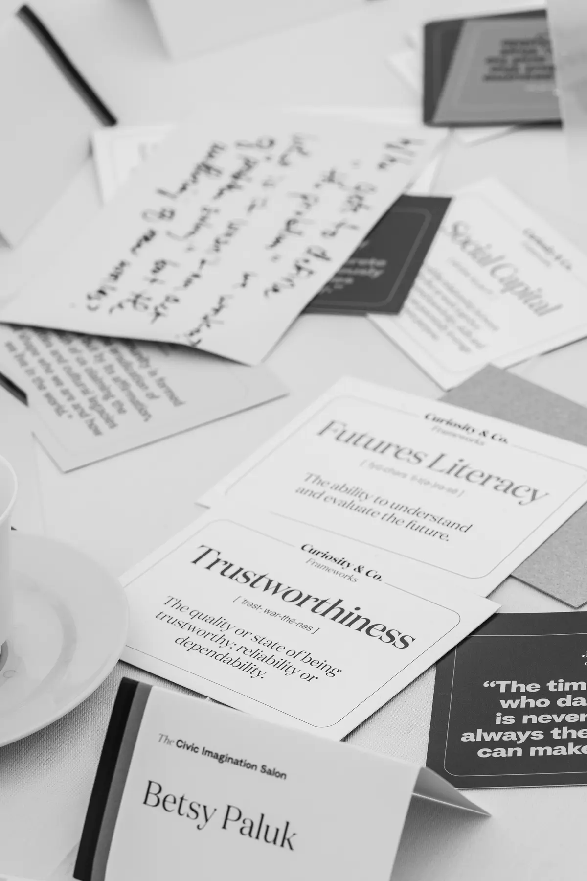 A table covered with thought-provoking quote cards, handwritten notes, and name placards, suggesting a reflective discussion or workshop setting. Small pumpkins, a cup of tea, and a set of Sharpie markers add warmth and creativity to the scene. Featured quotes from James Baldwin and bell hooks highlight themes of change, trust, and the power of art.