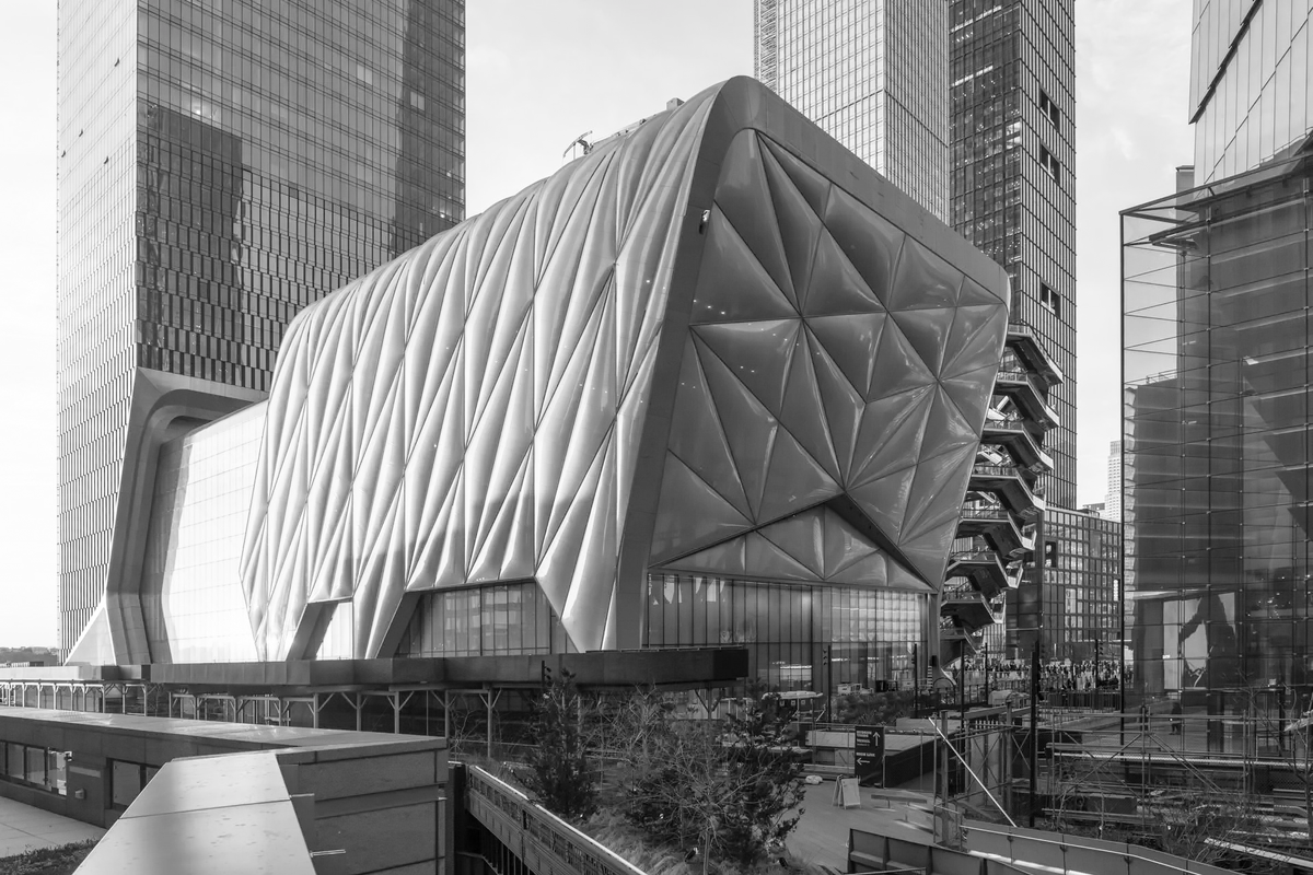 Black and white view of The Shed, a futuristic cultural center in Hudson Yards, New York City, with its distinctive quilted facade, surrounded by modern glass skyscrapers and adjacent to the Vessel sculpture.