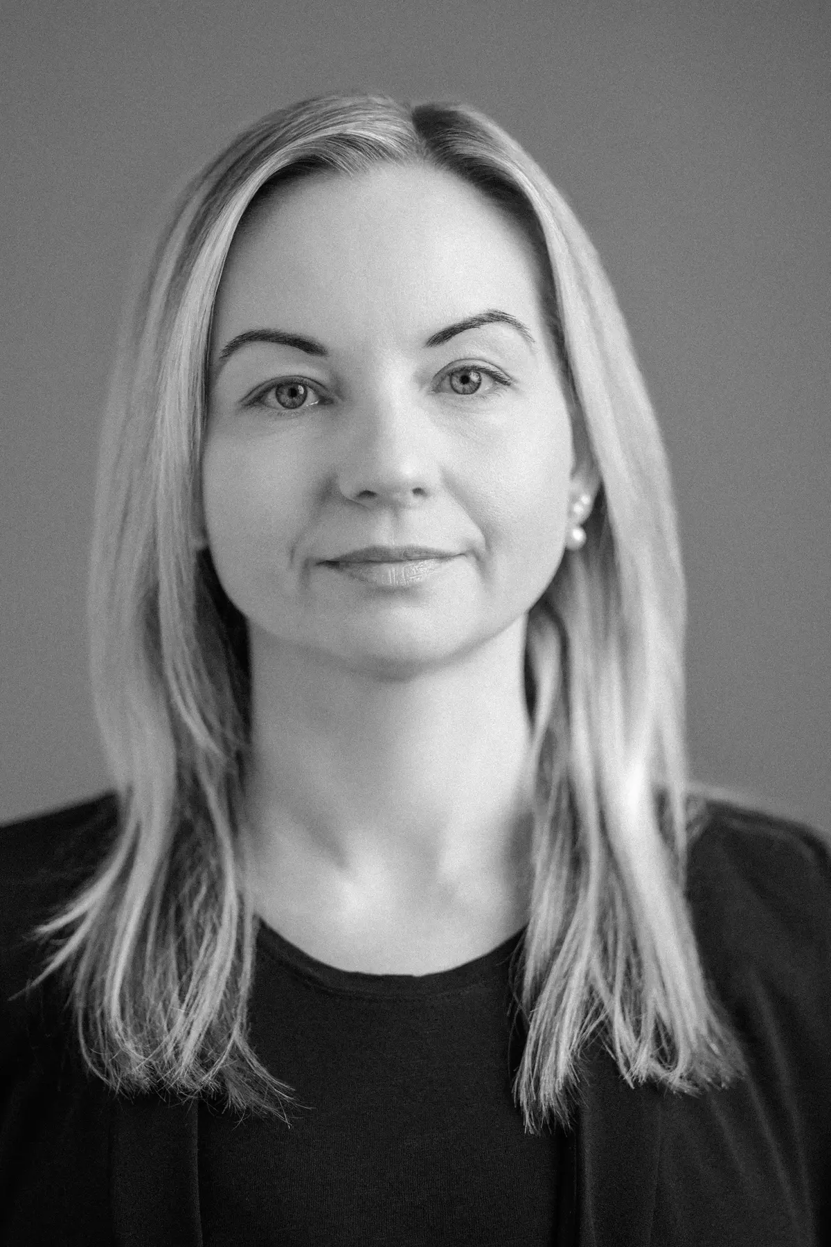 Lina Tamulyne with a confident expression, wearing professional attire, photographed from the shoulders up in a minimalist studio setting.
