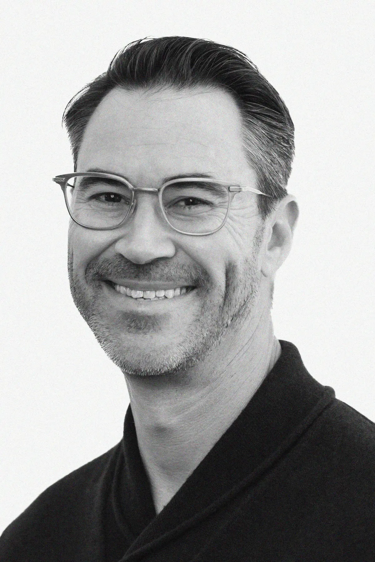 Todd Spector in a black-and-white portrait, gazing confidently at the camera with a smile against a soft white background.