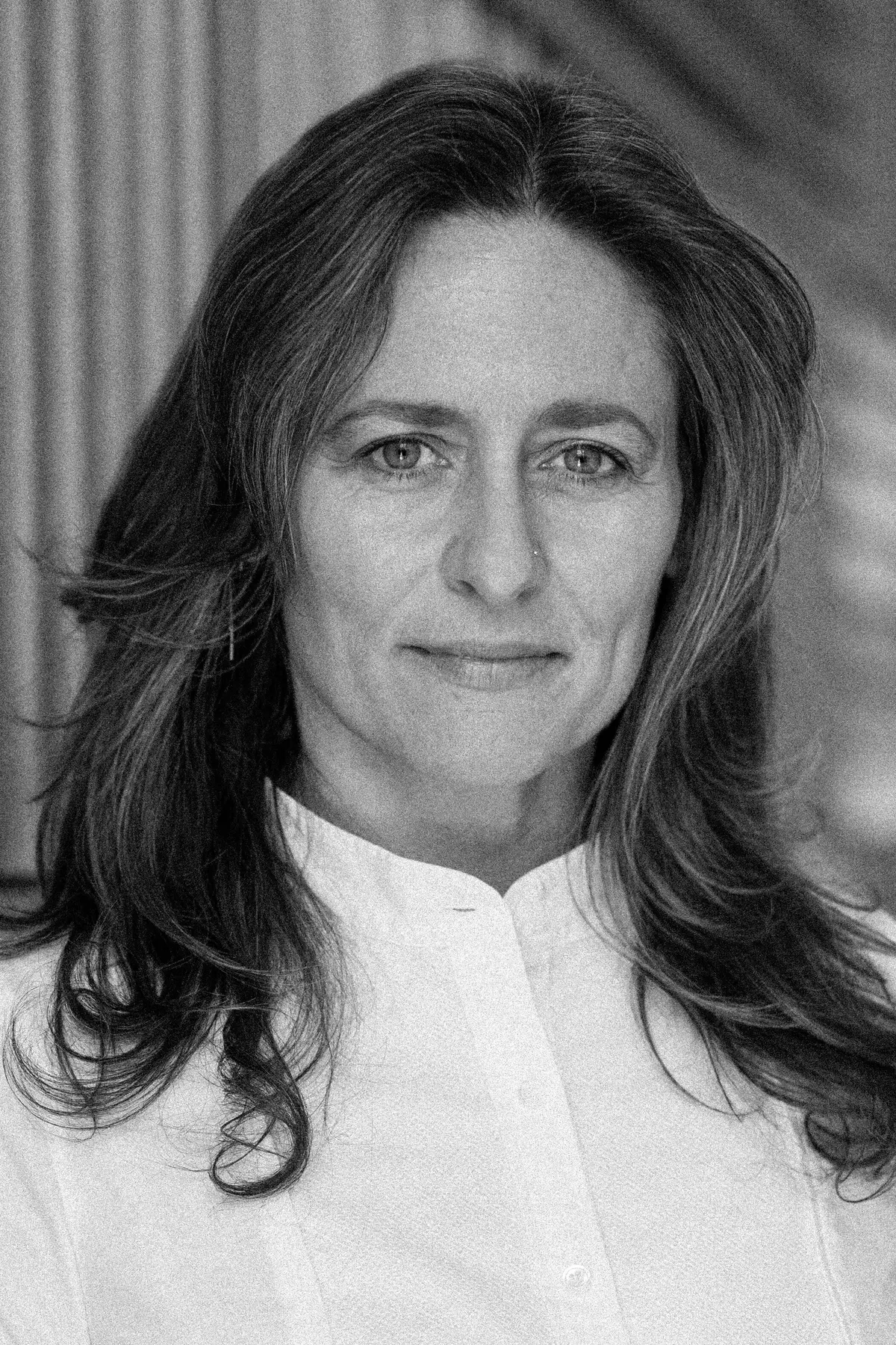 Betsy Levy Paluck in a black-and-white portrait, standing confidently in a modern, softly lit hallway, wearing a white button-down shirt with a calm and composed expression.
