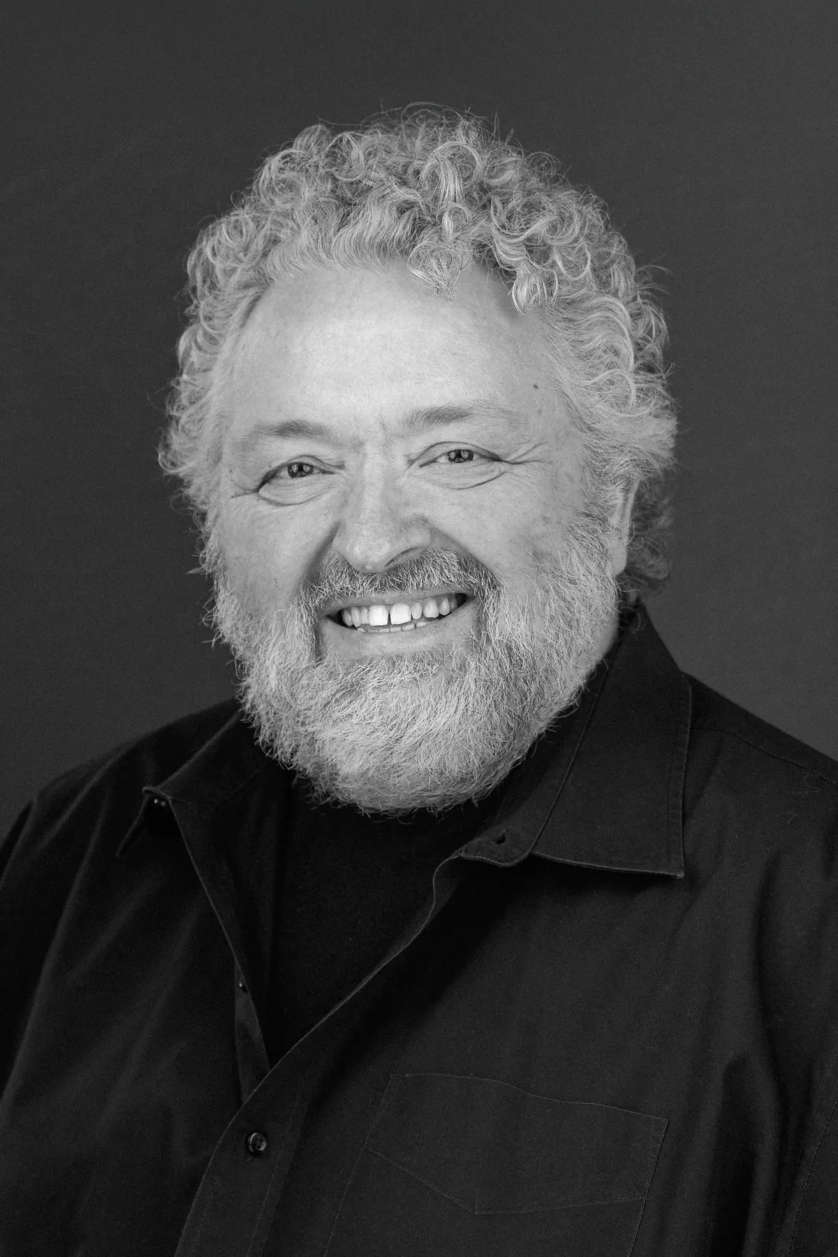 Bruce Mau with a confident expression, wearing professional attire, photographed from the shoulders up in a minimalist studio setting.