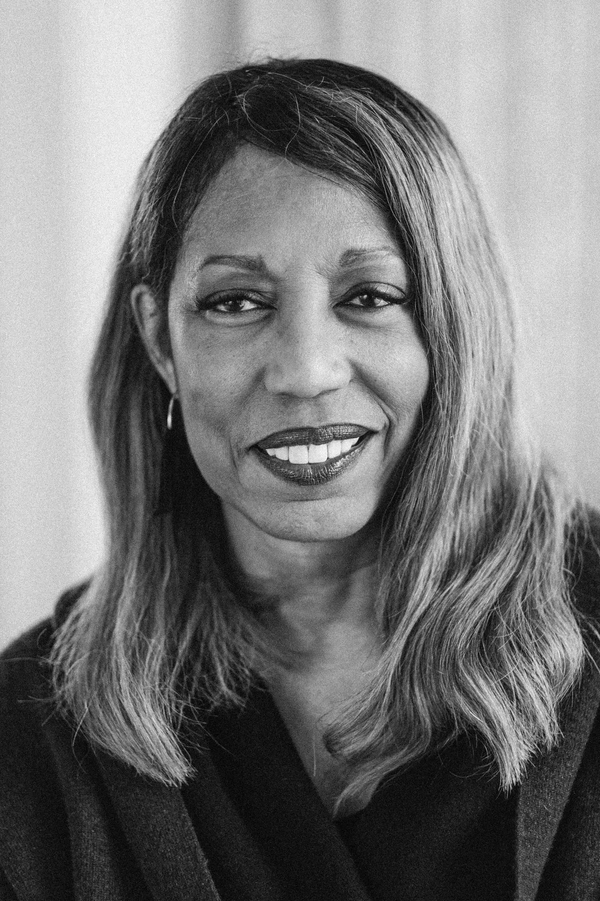 Denise Young in a black-and-white portrait, smiling warmly while wearing a dark shawl, with softly blurred vertical textures in the background.