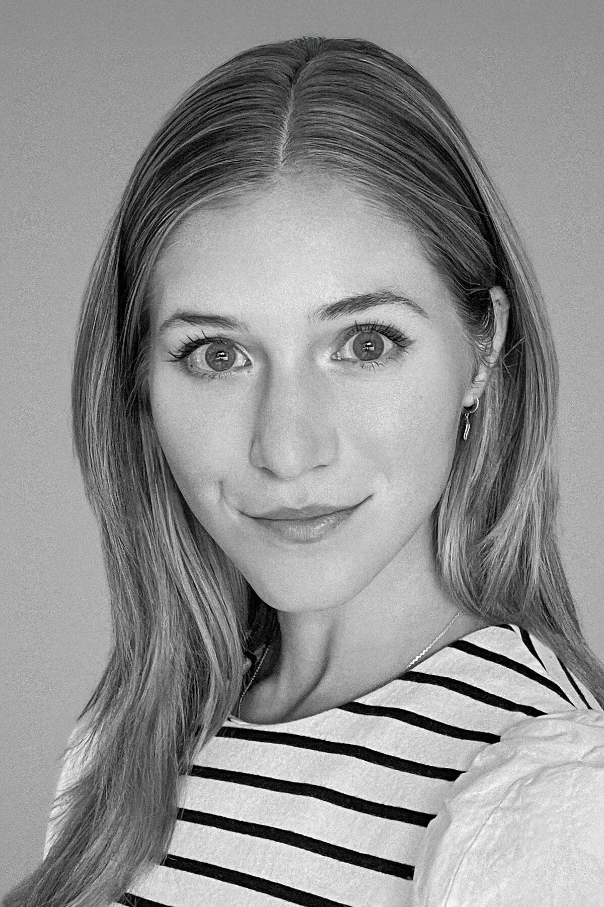 Grace Kay Matelich in a black-and-white portrait, gazing confidently at the camera with a subtle smile, wearing a striped top with puffed sleeves against a soft gray background.